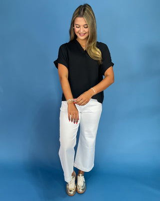 Woman wearing a black top and white pants against a blue background