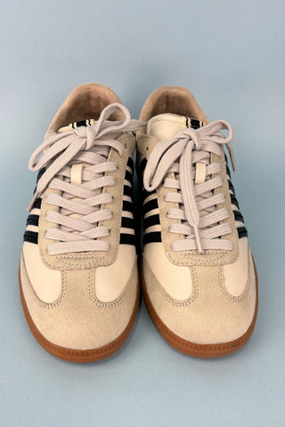 Pair of beige sneakers with black stripes on a light gray background