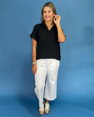 Woman wearing a black top and white pants against a blue background