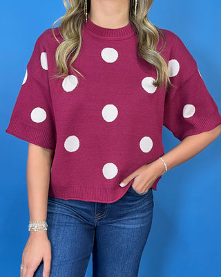 Burgundy short sleeve knit sweater top with oversized ivory polka dots, a round neckline, and ribbed trim.