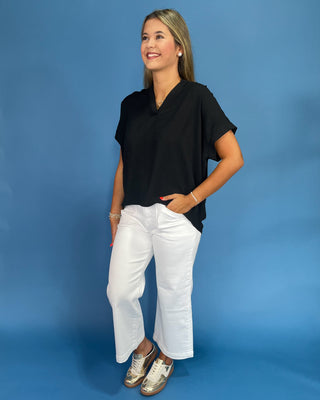 Woman wearing a black top and white pants against a blue background