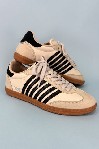 Pair of beige sneakers with black stripes on a light gray background