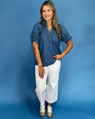 Woman wearing a blue blouse and white pants against a blue background