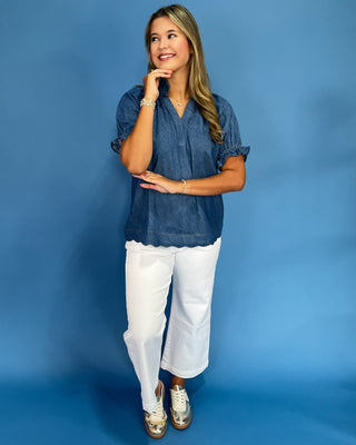 Woman wearing a blue blouse and white pants against a blue background