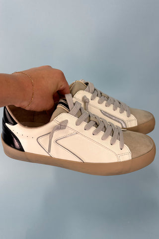 Beige and brown sneakers with a hand holding one shoe against a light blue background