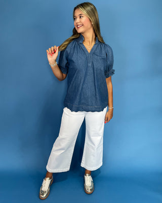 Woman wearing a blue blouse and white pants against a blue background
