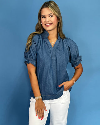 Woman wearing a blue blouse and white pants against a blue background