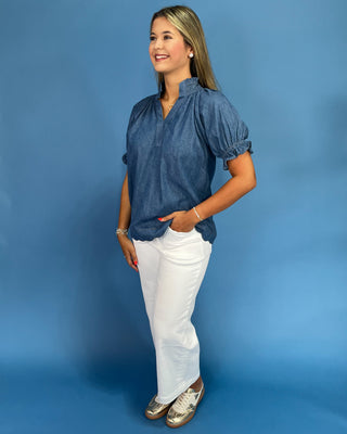 Woman wearing a blue blouse and white pants against a blue background