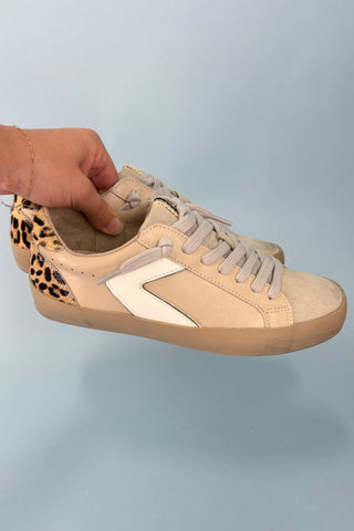 Beige sneaker with leopard print inner lining held by a hand against a light blue background