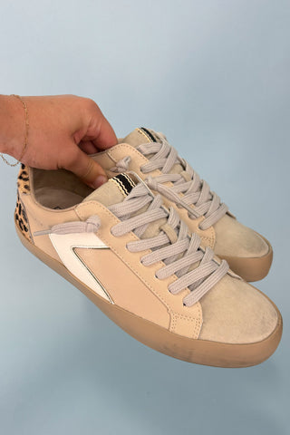 Beige sneaker with a white accent held by a hand against a light blue background