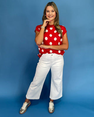 Woman wearing a red polka dot shirt and white pants against a blue background