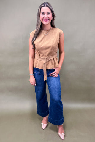 Woman wearing a beige sleeveless top and blue jeans against a plain background