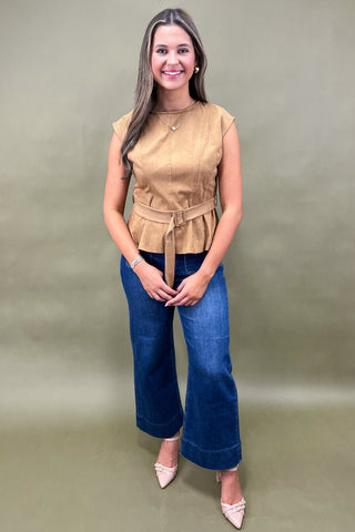 Woman wearing a beige sleeveless top and blue jeans against a plain background