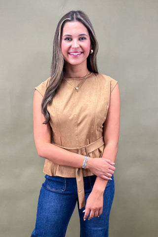 Woman wearing a beige sleeveless top and blue jeans against a plain background