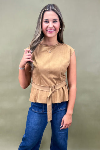 Woman wearing a beige peplum top and blue jeans against a plain background