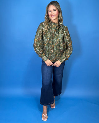 Olive green floral print long sleeve blouse with a ruffled neckline, statement bow detail, and warm brown and sage accents.