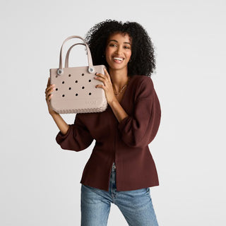 Woman holding a beige handbag with a visible brand logo against a light gray background