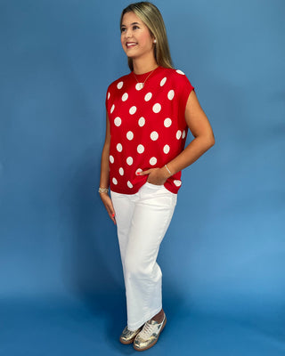 Woman wearing a red polka dot shirt and white pants against a blue background