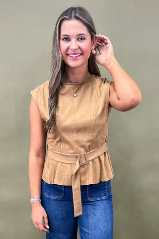 Woman wearing a tan peplum top and blue jeans against a green background