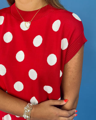 Red sweater with white polka dots worn by a person against a blue background