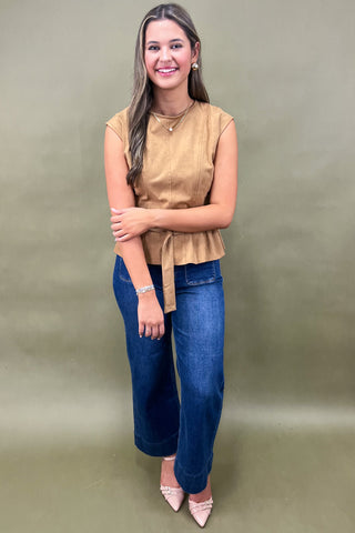 Woman wearing a beige top and blue jeans against a green background
