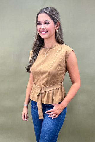 Woman wearing a beige sleeveless top with a belt and blue jeans against a green background