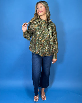 Olive green floral print long sleeve blouse with a ruffled neckline, statement bow detail, and warm brown and sage accents.