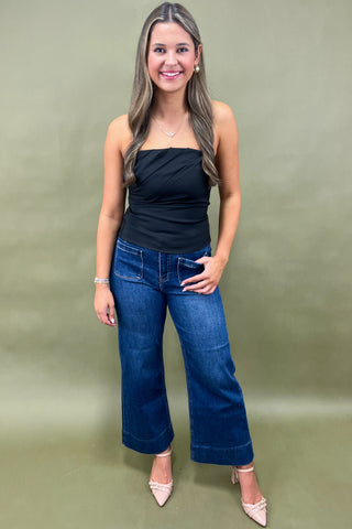 Woman wearing a black top and blue jeans against a green background