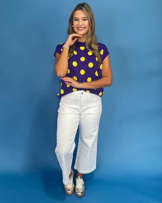Woman wearing a purple shirt with yellow polka dots and white pants against a blue background
