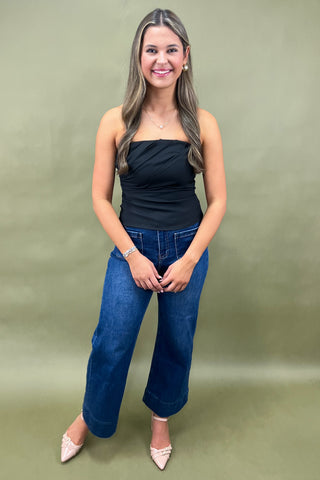 Woman wearing a black top and blue jeans against a green background