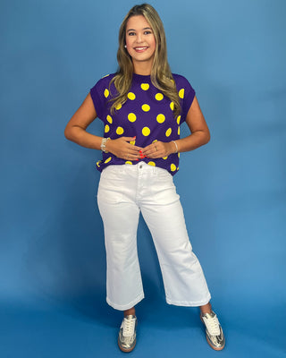 Woman wearing a purple top with yellow polka dots and white pants against a blue background