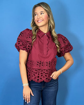 Burgundy eyelet blouse with statement puff sleeves, a collared neckline, scalloped trim, and intricate floral cutout details.