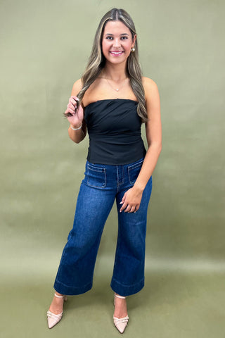 Woman wearing a black top and blue jeans against a green background