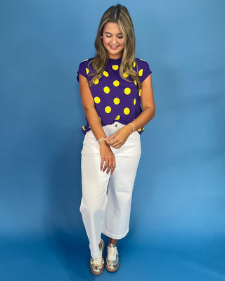 Woman wearing a purple top with yellow polka dots and white pants on a blue background