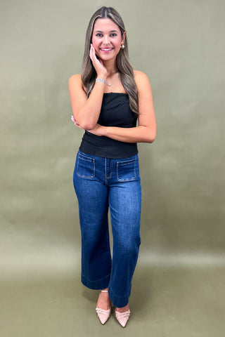Woman wearing a black top and blue jeans against a green background