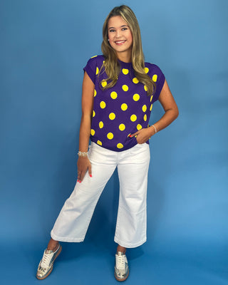Woman wearing a purple shirt with yellow polka dots and white pants on a blue background