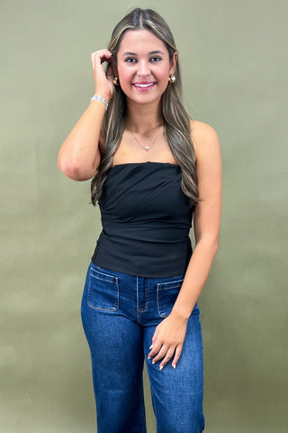 Woman wearing a black top and blue jeans against a green background