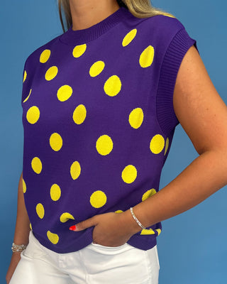 Purple sleeveless top with yellow polka dots worn by a person against a blue background
