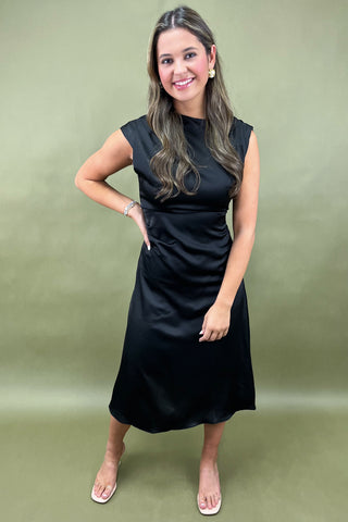 Woman wearing a black sleeveless dress against a green background