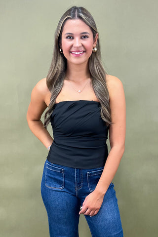 Woman wearing a black strapless top and blue jeans against a green background