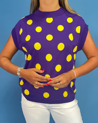 Person wearing a purple sleeveless top with yellow polka dots against a blue background