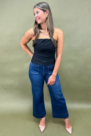 Woman wearing a black top and blue jeans against a green background