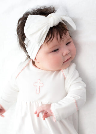 Baby wearing a white outfit with a pink flower design and a white headband on a white background