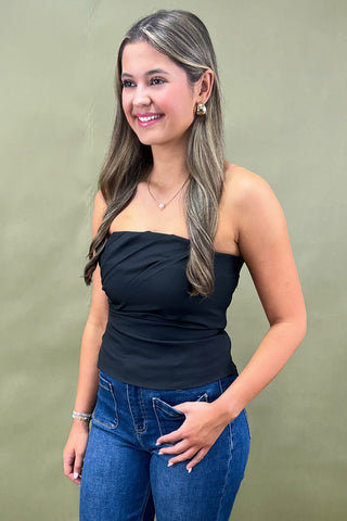 Woman wearing a black strapless top and blue jeans against a green background