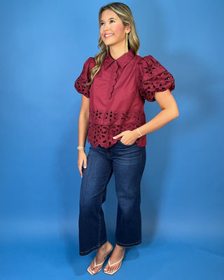 Burgundy eyelet blouse with statement puff sleeves, a collared neckline, scalloped trim, and intricate floral cutout details.