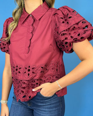 Burgundy eyelet blouse with statement puff sleeves, a collared neckline, scalloped trim, and intricate floral cutout details.