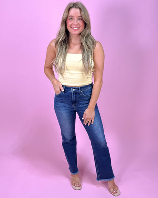 Woman wearing a yellow top and blue jeans against a pink background