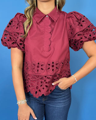 Burgundy eyelet blouse with statement puff sleeves, a collared neckline, scalloped trim, and intricate floral cutout details.
