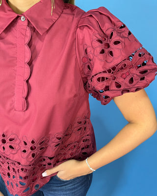 Burgundy eyelet blouse with statement puff sleeves, a collared neckline, scalloped trim, and intricate floral cutout details.