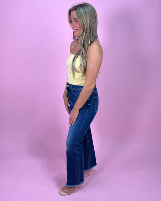Woman wearing a yellow top and blue jeans against a pink background